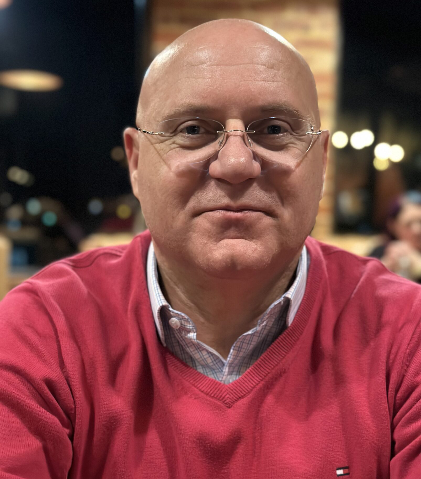 A man wearing glasses and a red sweater smiling at the camera.
